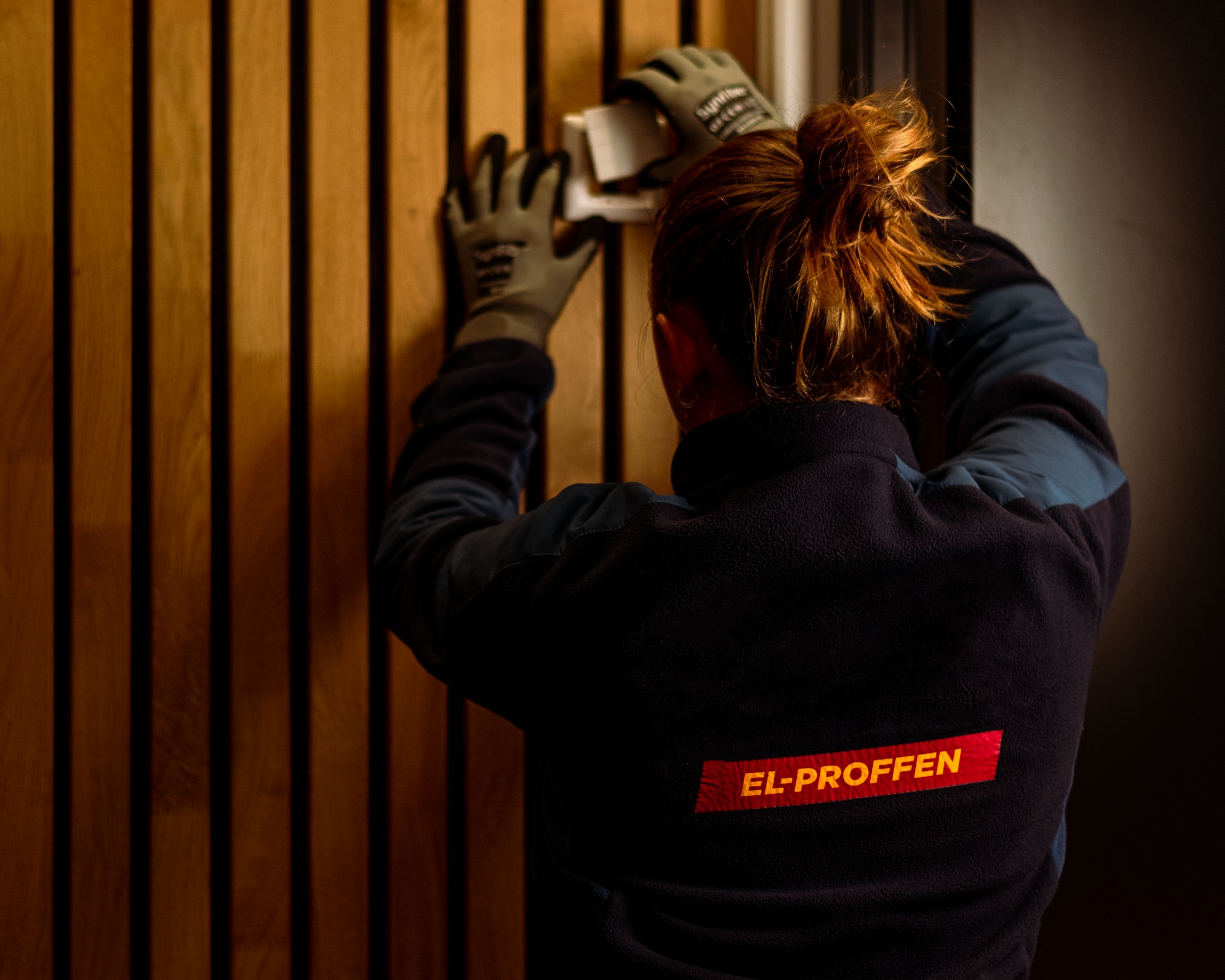 Kvinnelig elektriker ser på en stikkontakt på en spilevegg i en bolig