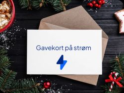 Et gavekort på et bord på en konvolutt hvor det står gavekort på strøm. I bakgrunnen ser man granbar, en kopp kakao og pepperkaker som bidrar til julestemning.