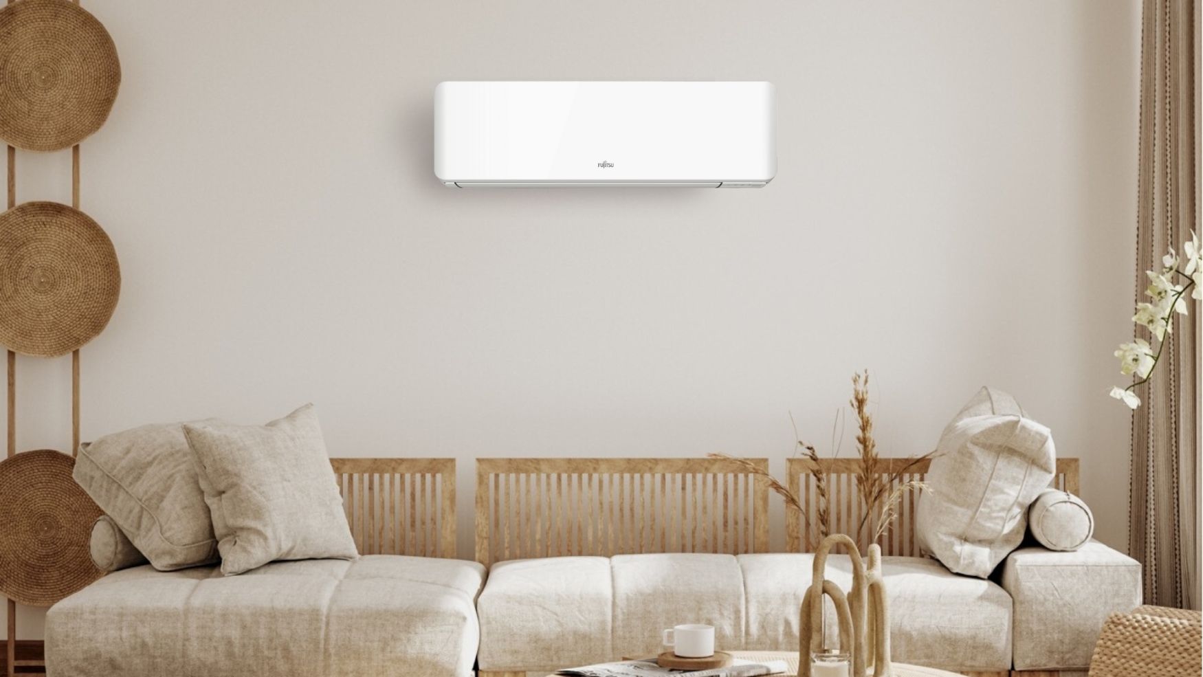 Varmepumpe i en innbydende og moderne stue med jordfarger og røffe tekstiler og materialer. Veggene er beige, og lyset flommer inn fra høyre. Varmpeumpen fra Fujitsu henger midt i rommet over sofaen, og man kan skimte sofabordet i forgrunnen.