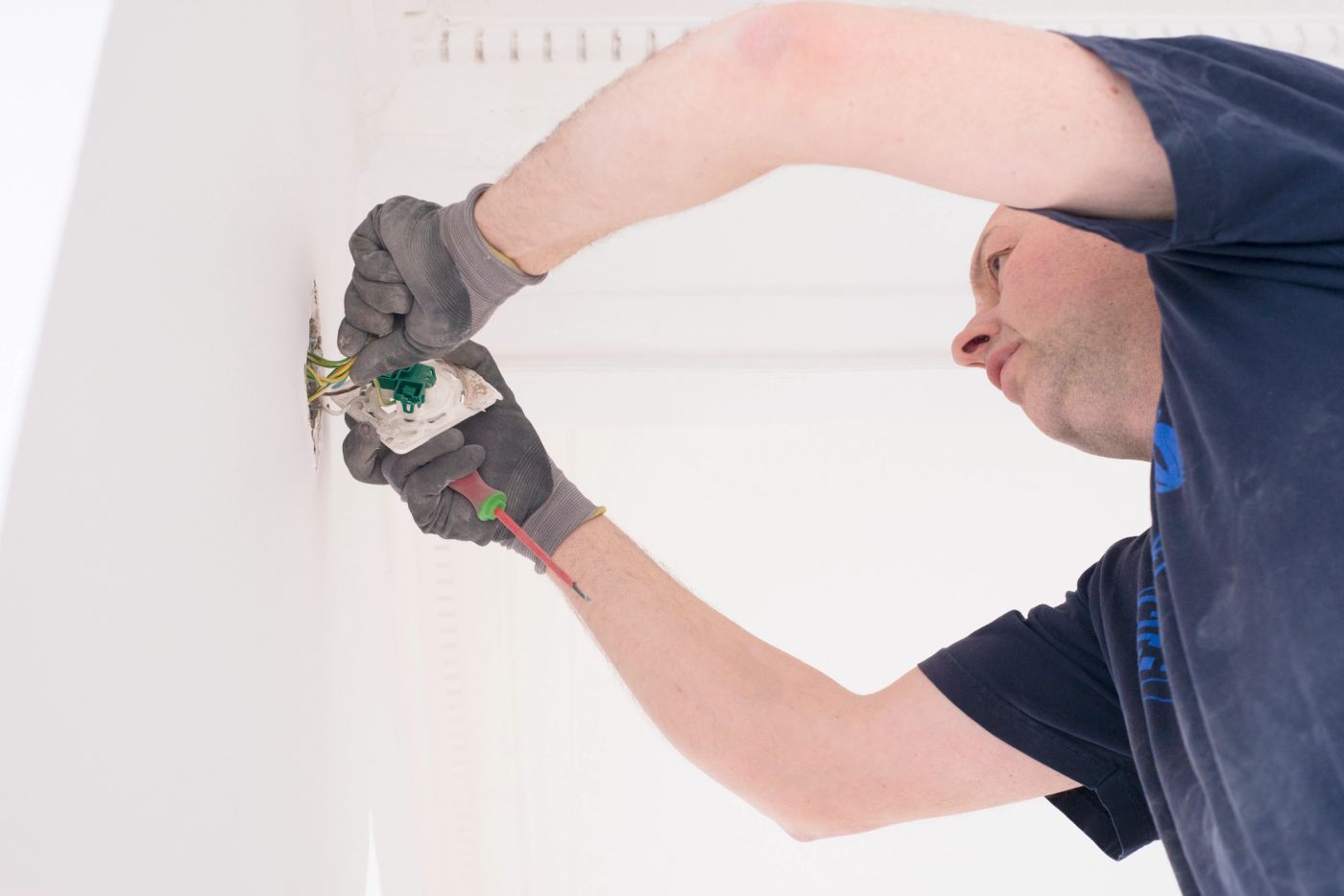 Elektriker med hansker kobler ledninger i en veggboks – typisk arbeid med stikkontakter eller brytere i privat bolig.