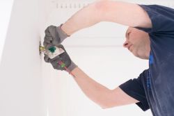 Elektriker med hansker kobler ledninger i en veggboks – typisk arbeid med stikkontakter eller brytere i privat bolig.