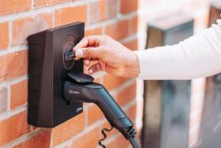 Nærbilde av Zaptec Go elbillader på murvegg – hånd holder Zaptec RFID-brikke for å starte trygg og kontrollert elbillading.