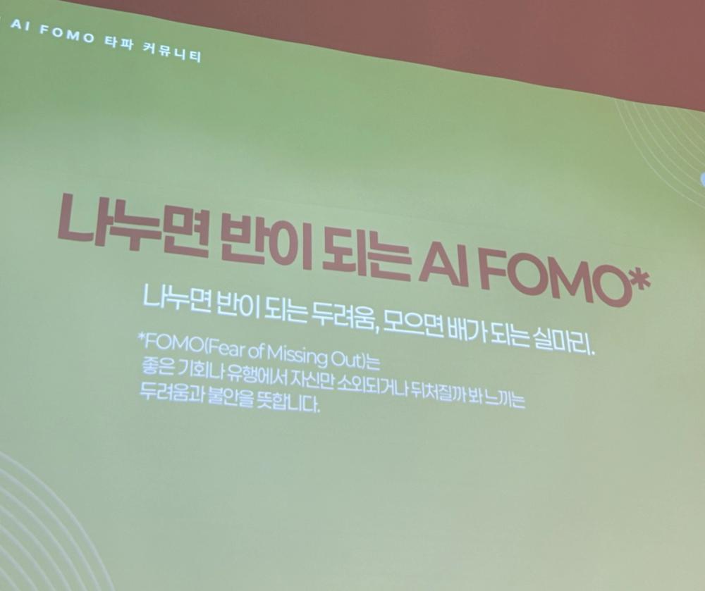 행사장 스크린의 슬라이드. 제목은 '나누면 반이 되는 AI FOMO', 부제는 '나누면 반이 되는 두려움, 모으면 배가 되는 실마리'이며 아래에 FOMO의 뜻을 설명하는 각주가 있다.