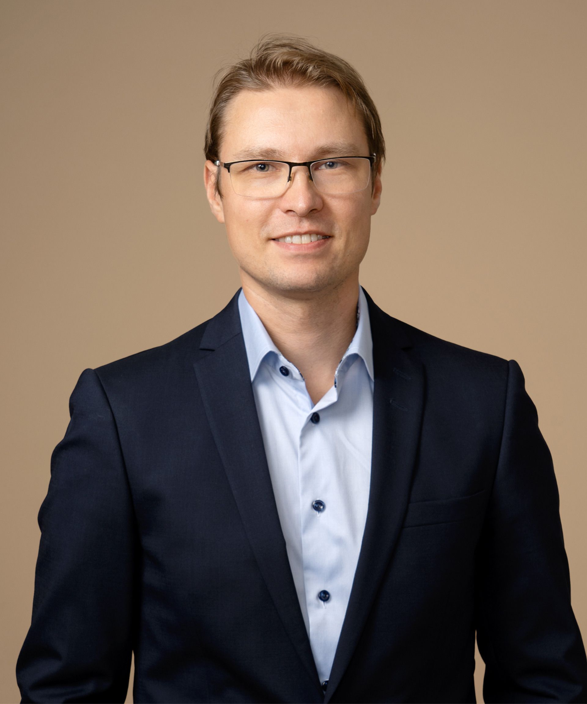 Person with glasses and short hair in dark suit with blue collar shirt