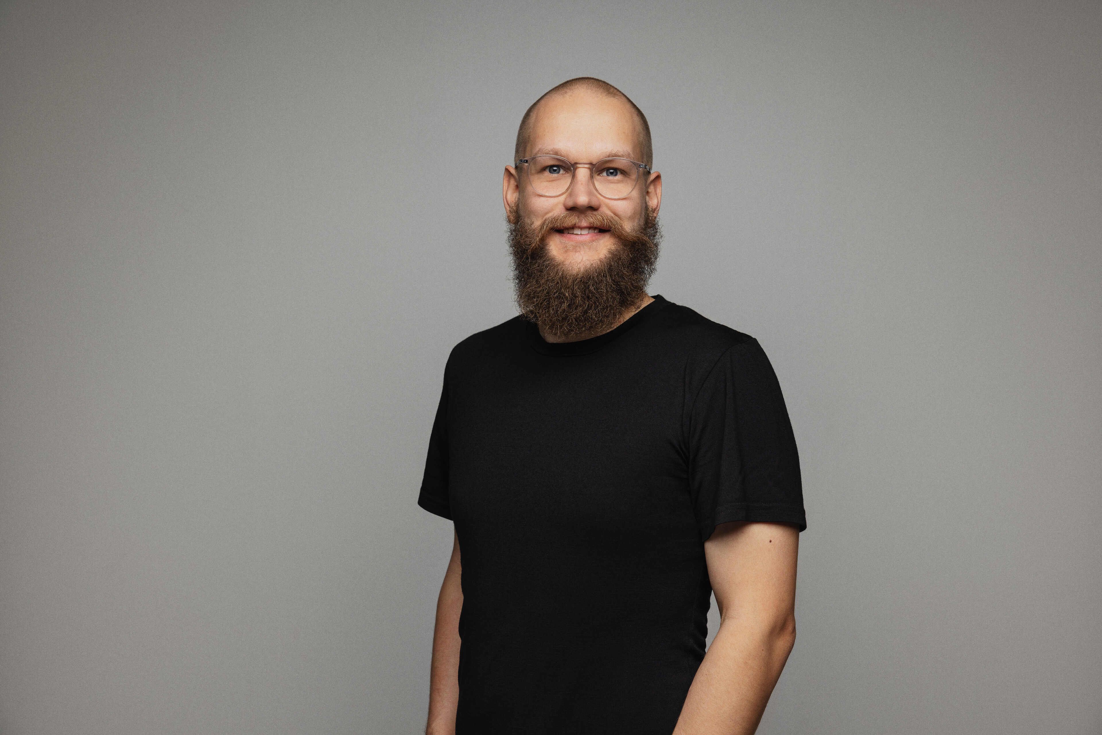 A smiling bald man with a brown beard in a black t-shirt