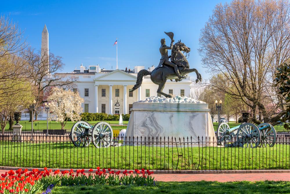 Vue de la Maison‑Blanche avec la statue équestre d’Andrew Jackson dans Lafayette Square, entourée de canons et d’arbres en fleurs.