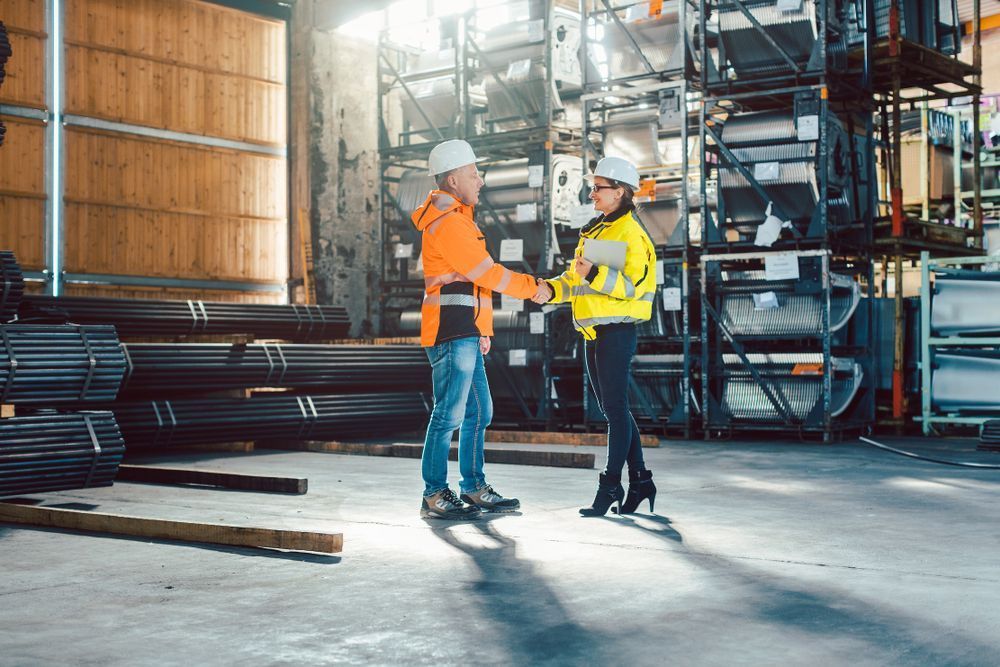 Two industrial workers in safety gear shaking hands in a warehouse setting