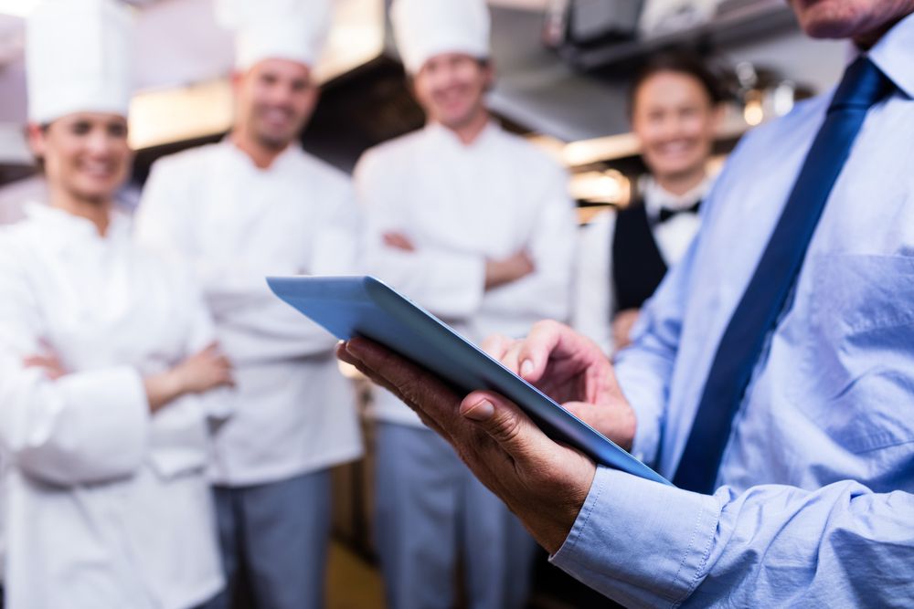 Restaurant manager using tablet with chefs and staff in background