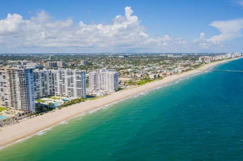Image of beachfront high-rise condos and turquoise ocean along Deerfield Beach, Florida under a bright blue sky.