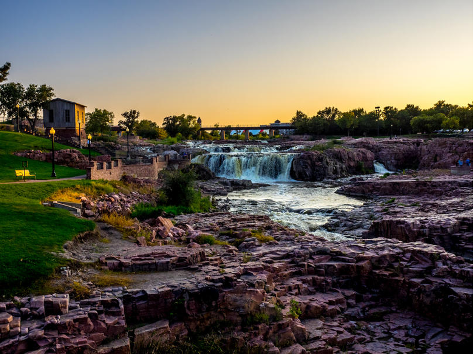 Falls Park waterfall surrounded by red rock formations and greenery at sunset in Sioux Falls, South Dakota