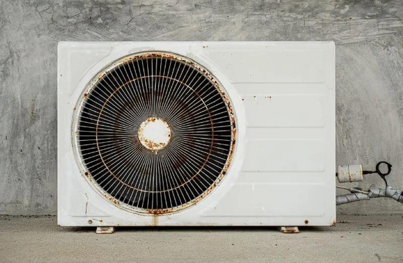 Image of a rusted and weathered outdoor AC condenser unit placed against a concrete wall.