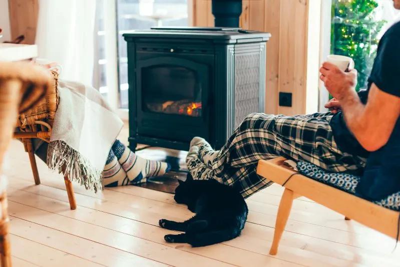 Guide de remplacement et de nettoyage des filtres d’humidificateur — image d’une personne en pyjama à carreaux relaxant avec une tasse près d’un foyer, un chat noir couché à proximité.
