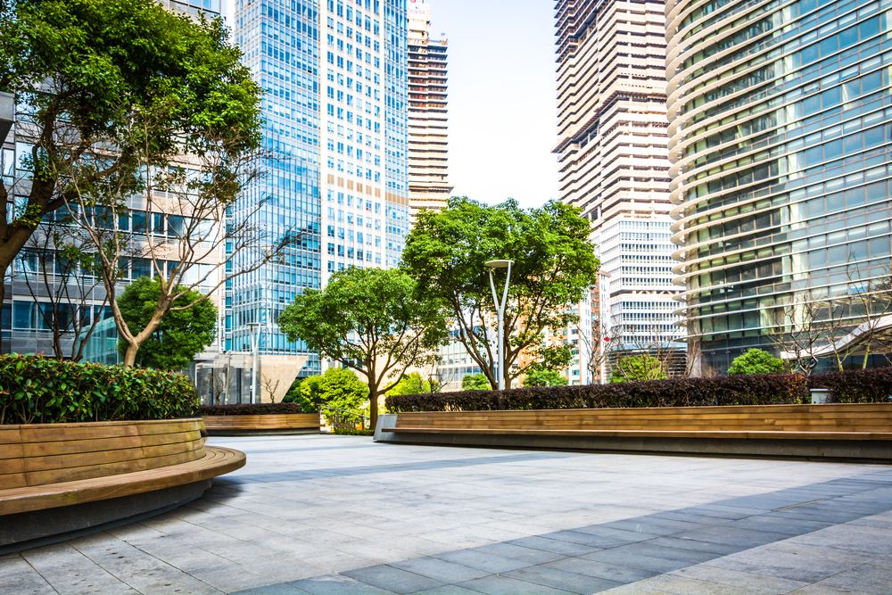 Urban business district with skyscrapers, trees, and empty public benches in a city plaza
