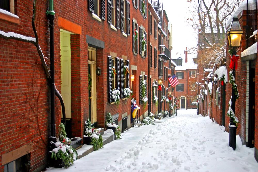 Snow-covered Acorn Street in Boston’s Beacon Hill with historic brick row houses decorated for winter.
