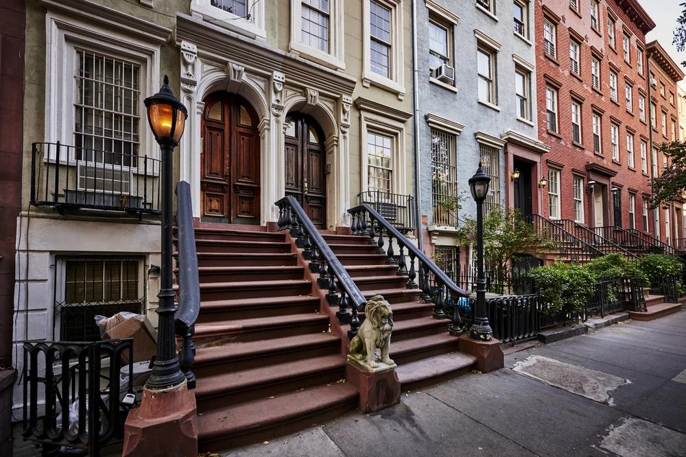 Historic brownstone row houses with stoops and decorative lion statues in Greenwich Village, New York City.