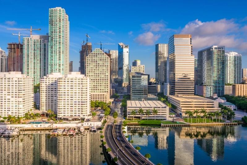 Villes comptant le plus de ménages multigénérationnels : image du centre‑ville de Miami montrant des immeubles modernes en hauteur se reflétant sur l'eau avec un ciel dégagé.