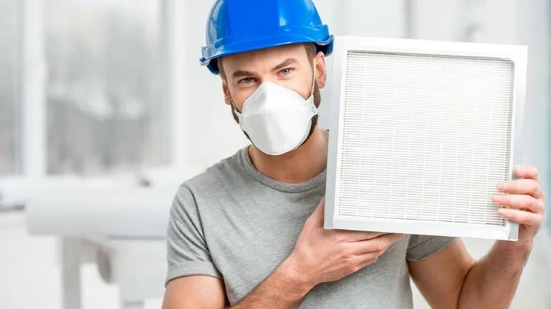 View of an HVAC expert holding an air filter that captures airborne particles in a house, which helps to prevent dusty rugs.