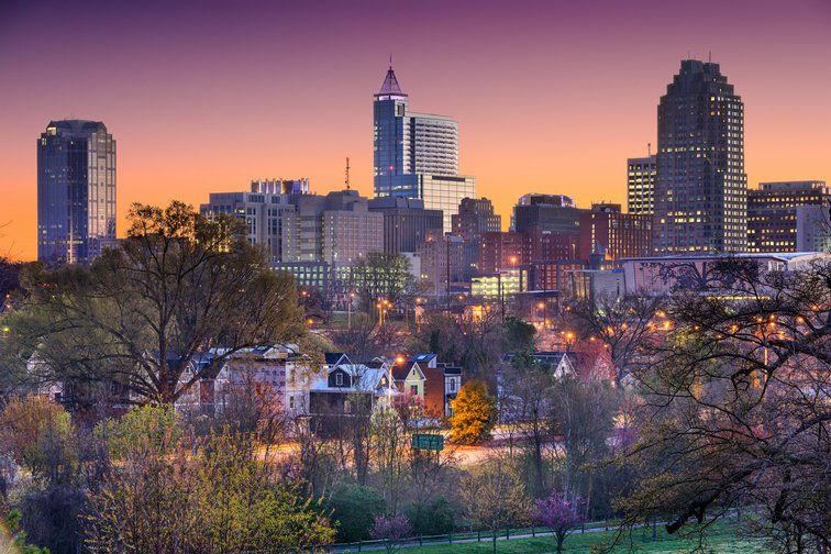 Sunset skyline featuring tall buildings and treetops under a colorful gradient sky.