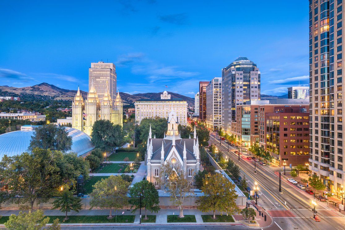 Urban skyline at dusk with historic buildings and tree-lined streets in the foreground.