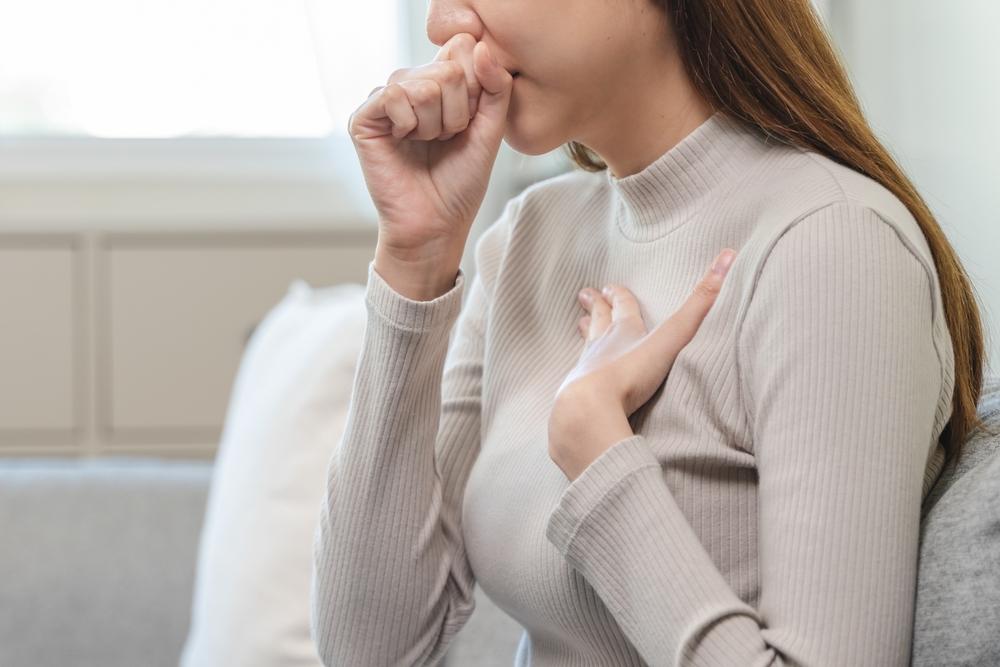 Vue d’une femme toussant la main sur la poitrine, montrant les effets d’une mauvaise qualité de l’air intérieur.