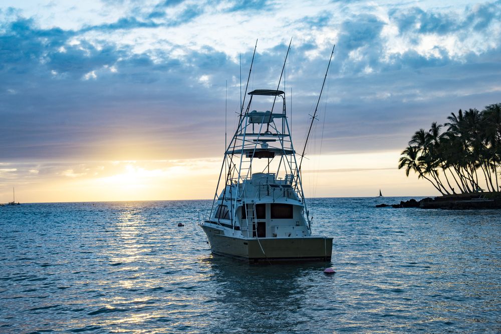 Sport fishing boat anchored in calm waters during a peaceful sunset with palm trees in the distance.