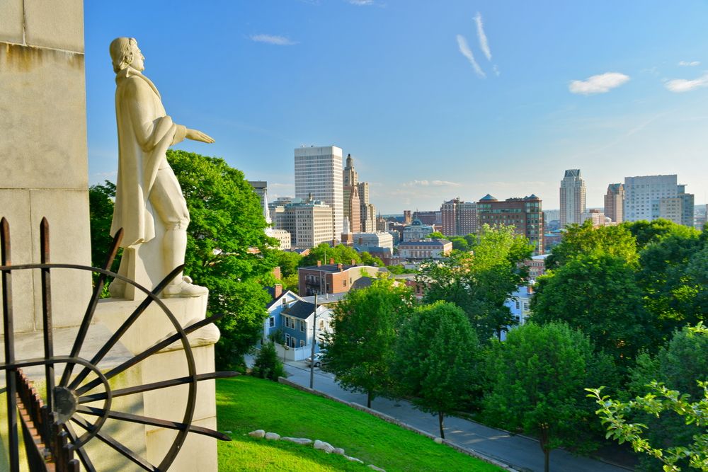 Marble statue overlooking a vibrant downtown cityscape with historic and modern buildings.