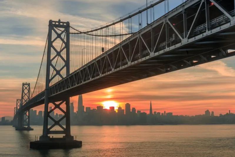 Vue de la silhouette de San Francisco au lever du soleil sous le Bay Bridge illustrant la forte disparité salariale des milléniaux locataires dans la ville.