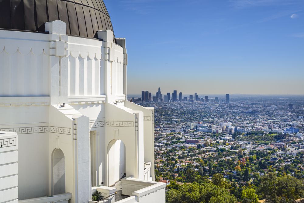 Iconic white observatory in the foreground with sprawling LA skyline in the distance.