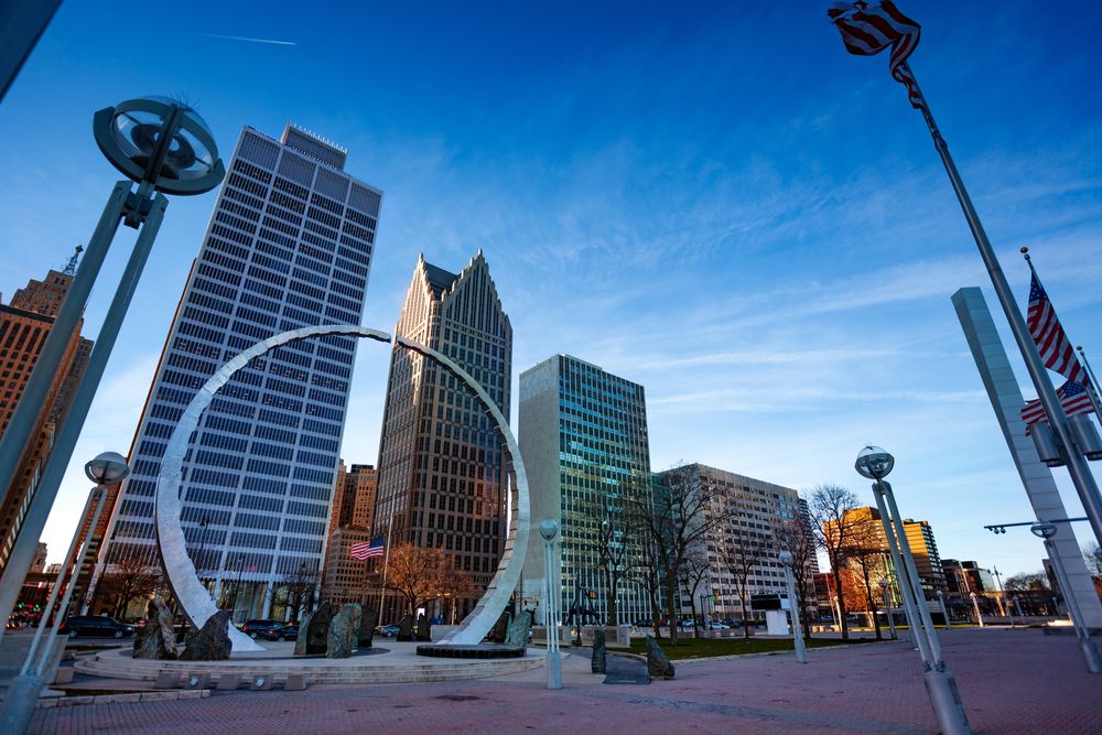Urban skyline at sunrise with a circular monument in the foreground.