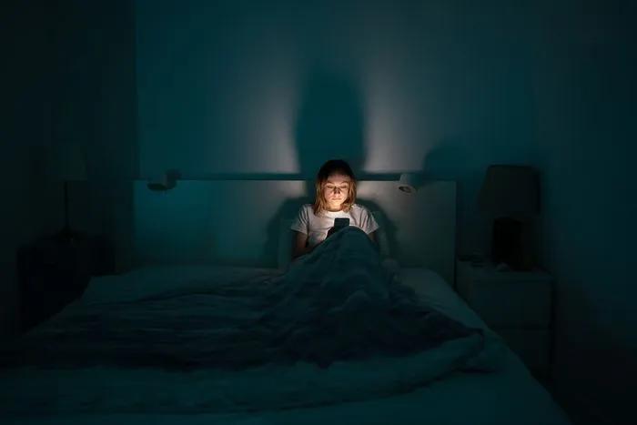 Femme utilisant son téléphone au lit la nuit — la mauvaise qualité de l’air et le temps d’écran peuvent perturber la santé du sommeil.