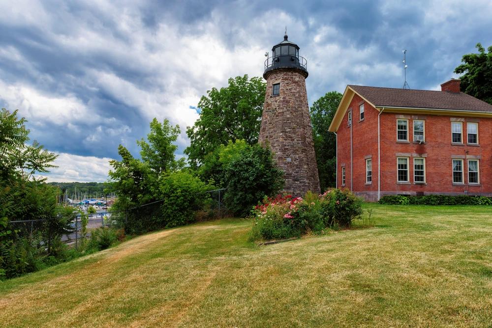 A view of the historic Sodus Bay Lighthouse and keeper’s house in upstate New York, surrounded by greenery and overlooking Lake Ontario.