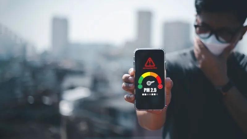 View of a man holding a smartphone that displays the PM2.5 level detector.