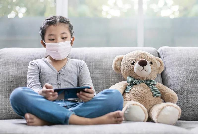 View of a child wearing face mask indoors with teddy bear, concerned about VOCs and indoor air quality.