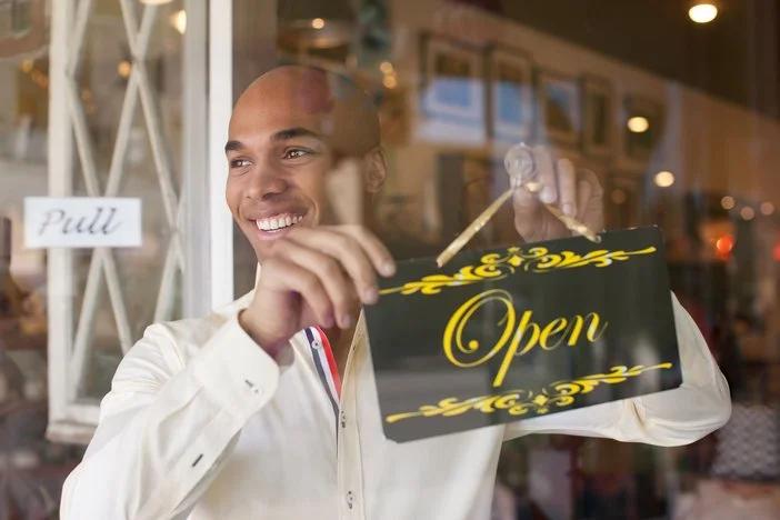 Image of a man happily turning the store's label signifiying that the store is open for doing business.