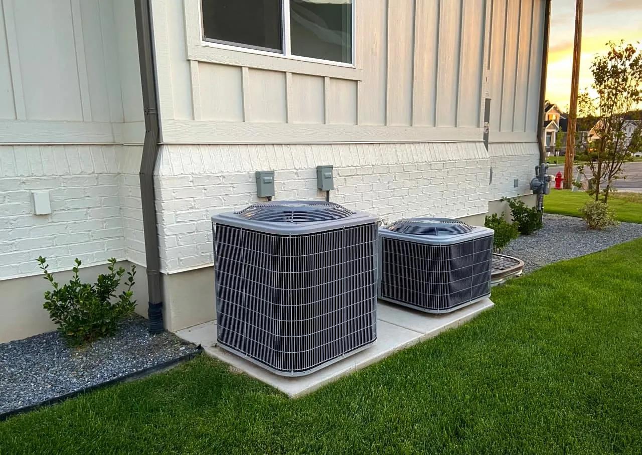 Two central air conditioning units installed outside a modern home with neatly landscaped surroundings