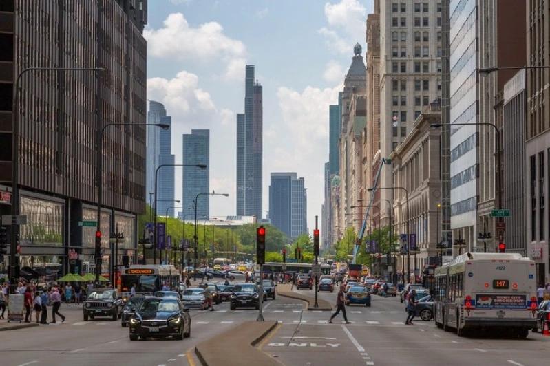 Cities Where Remote Workers Log the Most Hours - Images of the Chicago's downtown with traffic moving along the street, skyscrapers towering over the road, and pedestrians crossing at traffic lights.