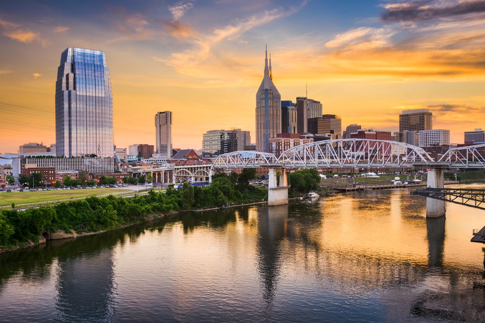 Nashville, Tennessee skyline at sunset with prominent AT&T Building and pedestrian bridge over the river.
