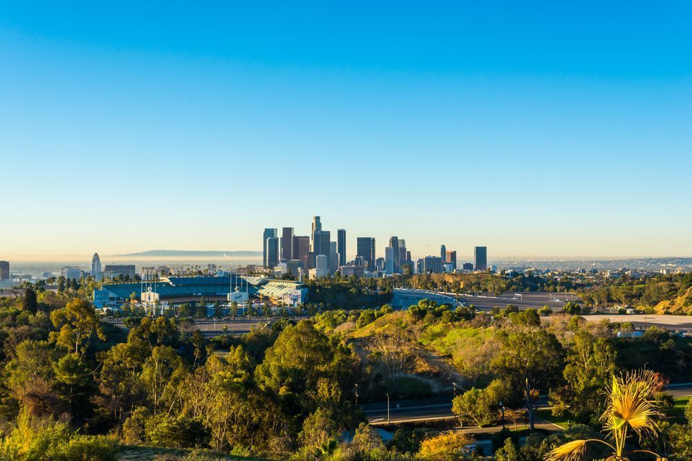 Skyline du centre‑ville de Los Angeles avec le Dodger Stadium et des collines boisées au premier plan.