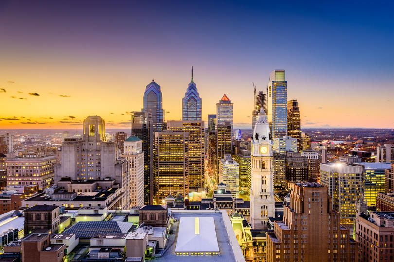 Riverfront city skyline at sunset with a prominent bridge and glass towers.