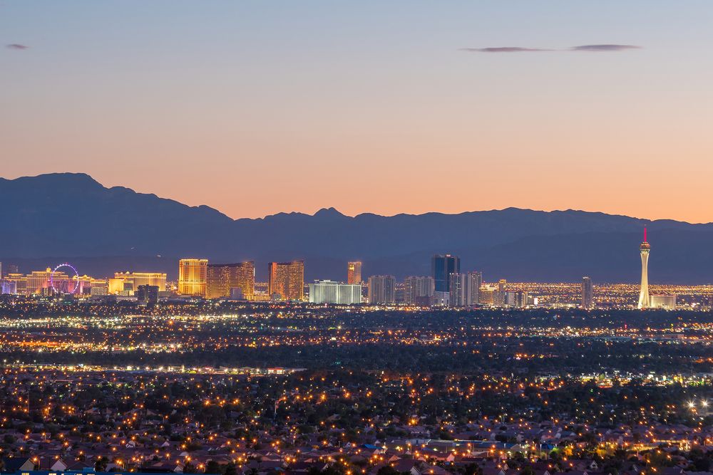 Distant view of the Las Vegas Strip glowing at dusk with mountains in the background.