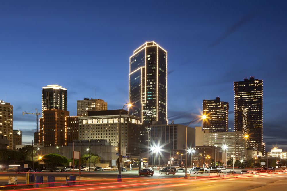 Fort Worth skyline lit up at night with streetlight and car trails.