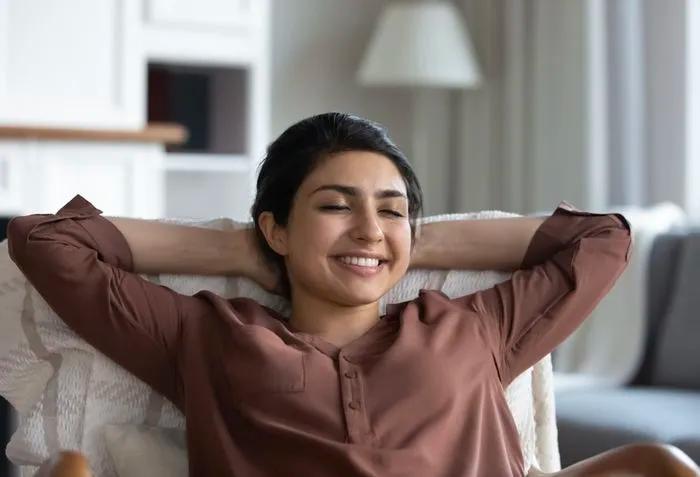 Une jeune femme souriante les mains derrière la tête, se détendant dans un salon douillet.