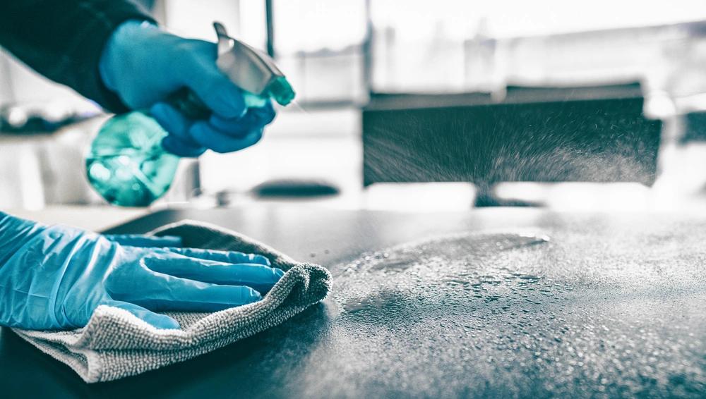 Gloved hands disinfecting a surface to reduce allergens and maintain a clean, healthy living space.