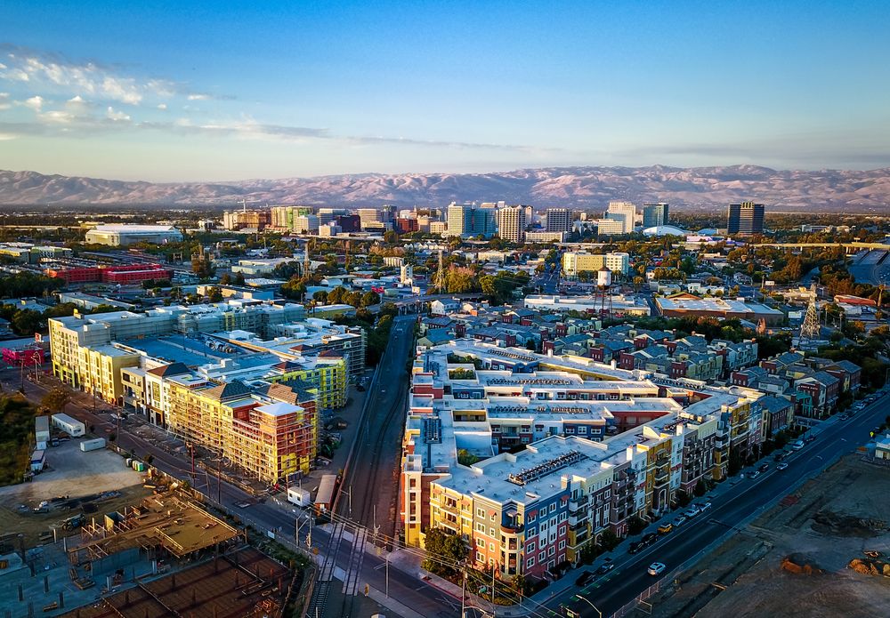Aerial view of colorful buildings and downtown skyline in San Jose, California, with surrounding mountains.