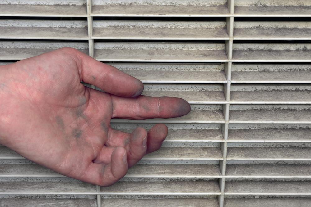 View of a hand covered in dust from a dirty air vent, illustrating neglected air filter maintenance.
