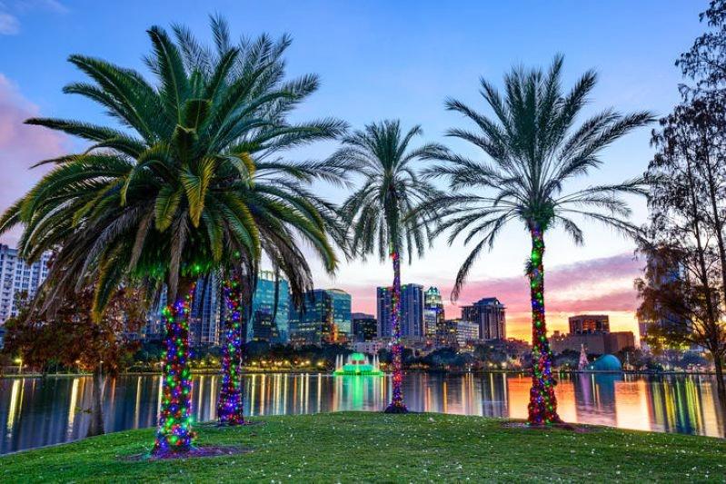 Cities Where Remote Workers Log the Most Hours - Images of the Orlando cityscape with palm trees lit up in Christmas lights, overlooking the lake with colorful reflections and the downtown skyline in the background.