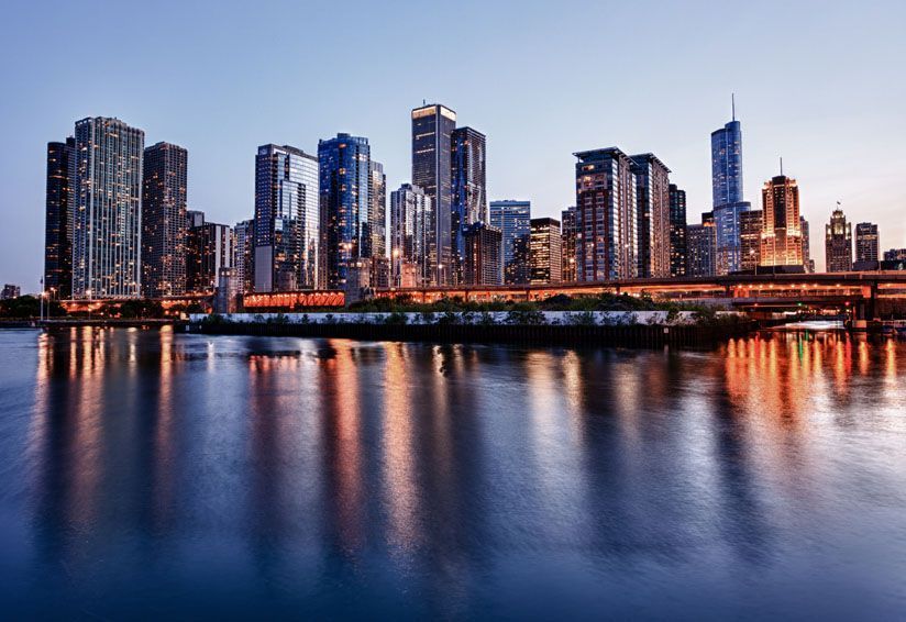 Paysage urbain de Chicago illuminé au crépuscule, montrant de hauts gratte‑ciel se reflétant dans la rivière, illustrant un environnement urbain animé pouvant poser des enjeux de qualité de l’air.