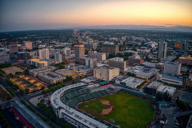 Villes comptant le plus de ménages multigénérationnels : image aérienne de Fresno, Californie, avec les immeubles du centre‑ville et un stade de baseball au coucher du soleil, montrant la ligne d'horizon de la ville.