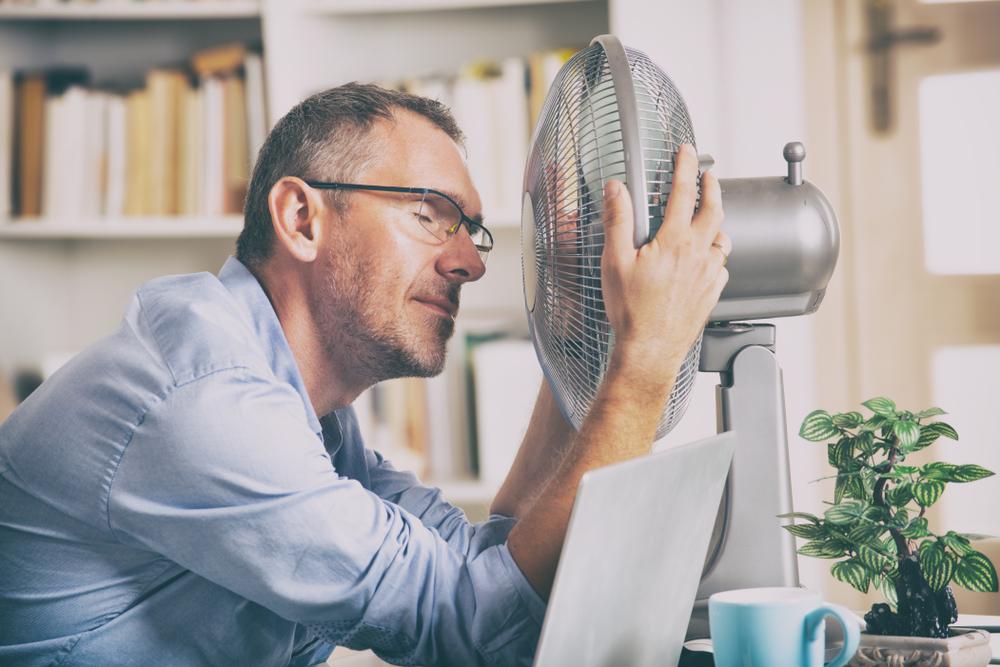 Image d’un homme agrippant les côtés d’un ventilateur électrique pour simplement se rafraîchir à cause de la chaleur intense.