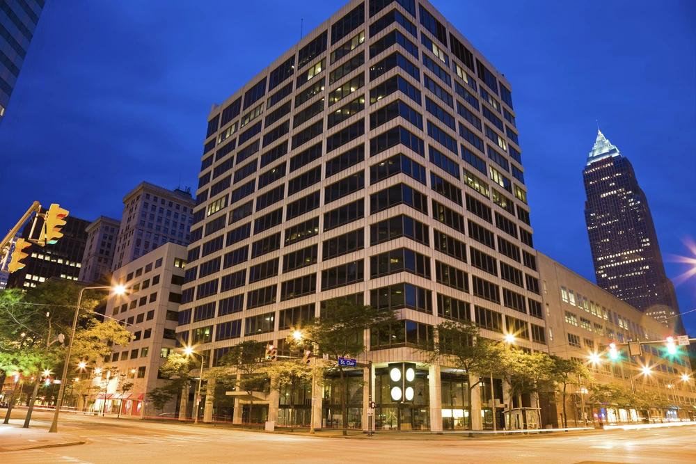 Image of downtown Cleveland office buildings at night with illuminated street lights and the Key Tower in the background.